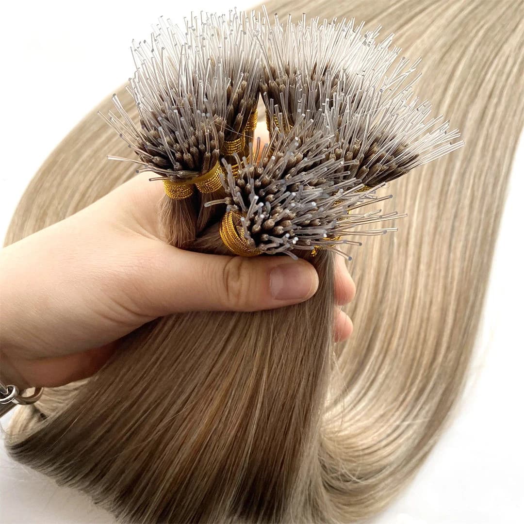 A hand holding blonde nano extension bundles with metal-loop tips visible