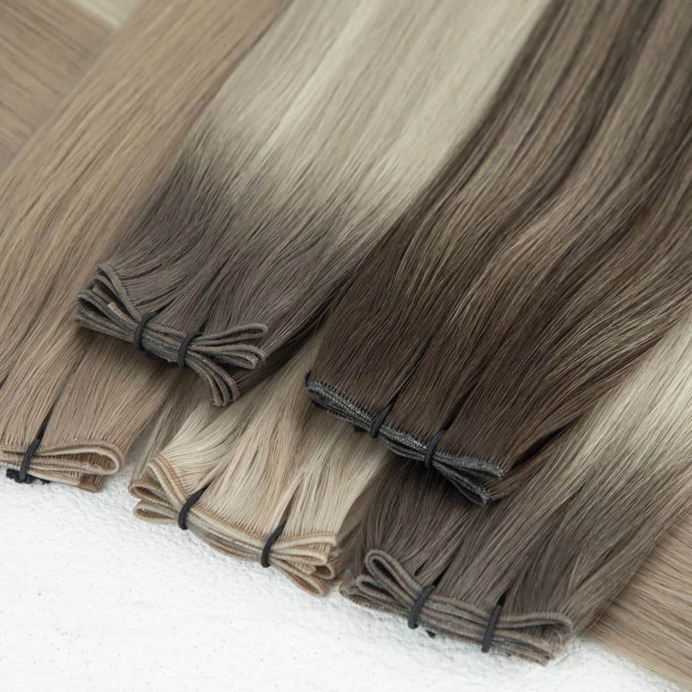 Blonde and brown hair extension bundles with visible folded weft seams on a light surface