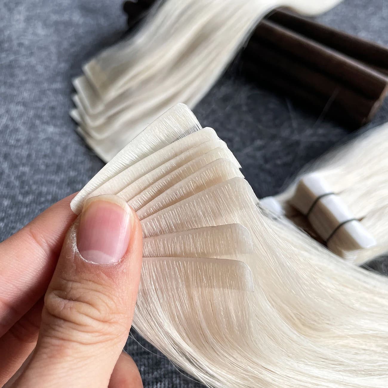 A hand holding pale blonde tape-in tabs with the root areas fanned out for a close-up