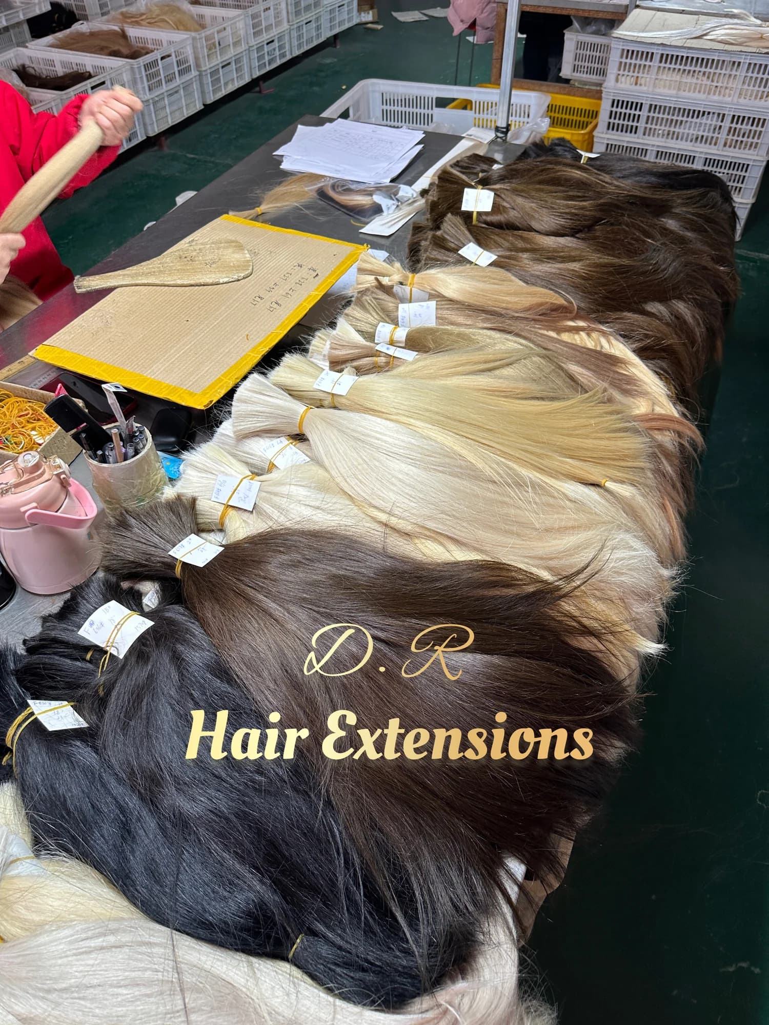 A worker handling lightened hair beside arranged bundles in DR Hair Extension's production area
